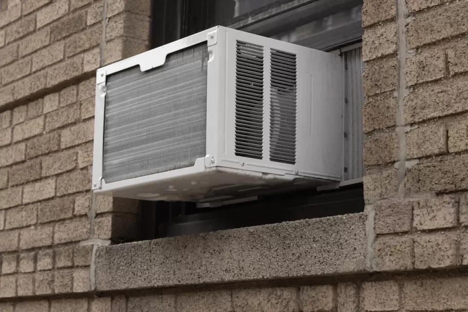 Close-up of white air conditioning window unit in window of brown brick building.